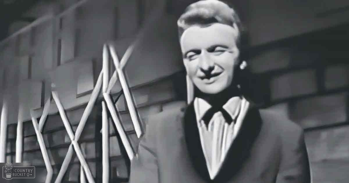 A young adult male wearing a classic mid-20th century suit jacket and bow tie in an urban outdoor setting with modern glass and metal architecture, black and white photograph.