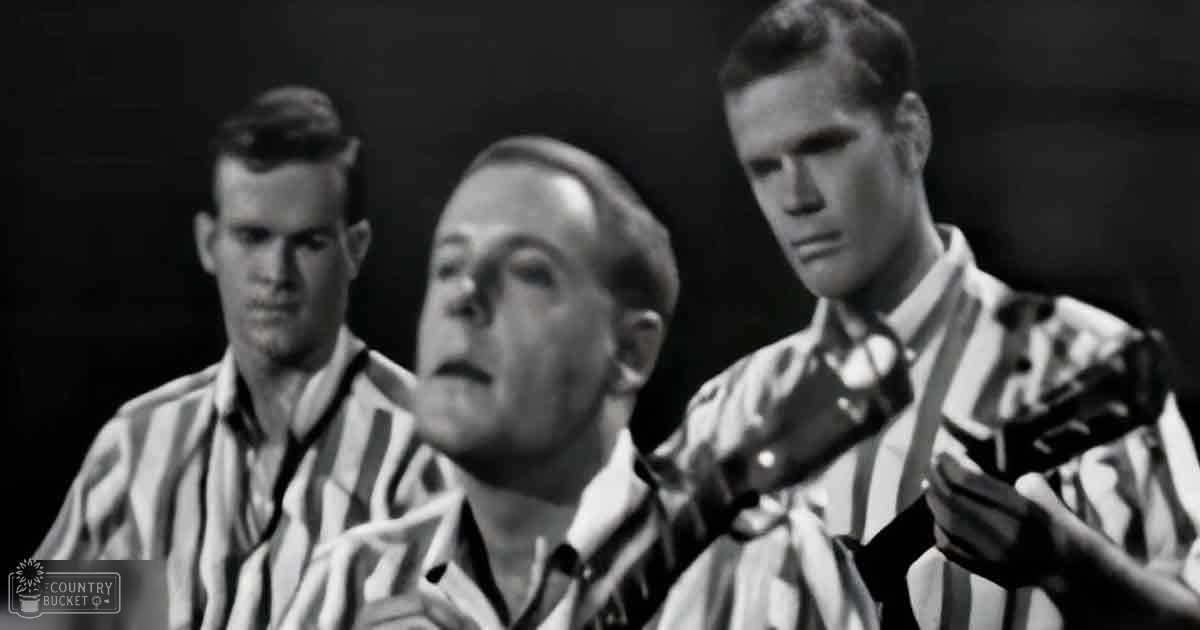 A group of men wearing prison uniforms, likely from a historical film set in a dark background with no season or time of day indicated by lighting.