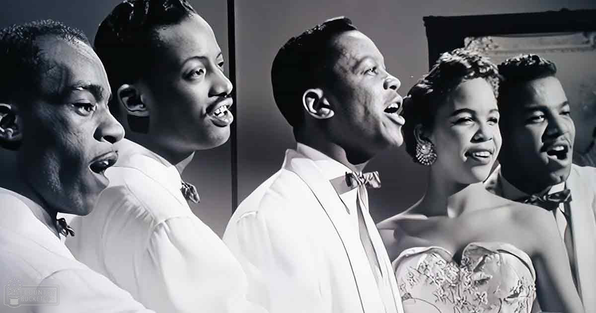 A group of adults singing in a studio setting with neutral tones, possibly from the mid-20th century based on their fashion and hairstyle styles.