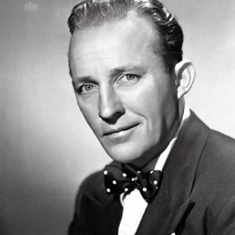 An adult male wearing a dark suit jacket, white polka-dotted bow tie, standing against a plain light backdrop in what appears to be a professional portrait setup.