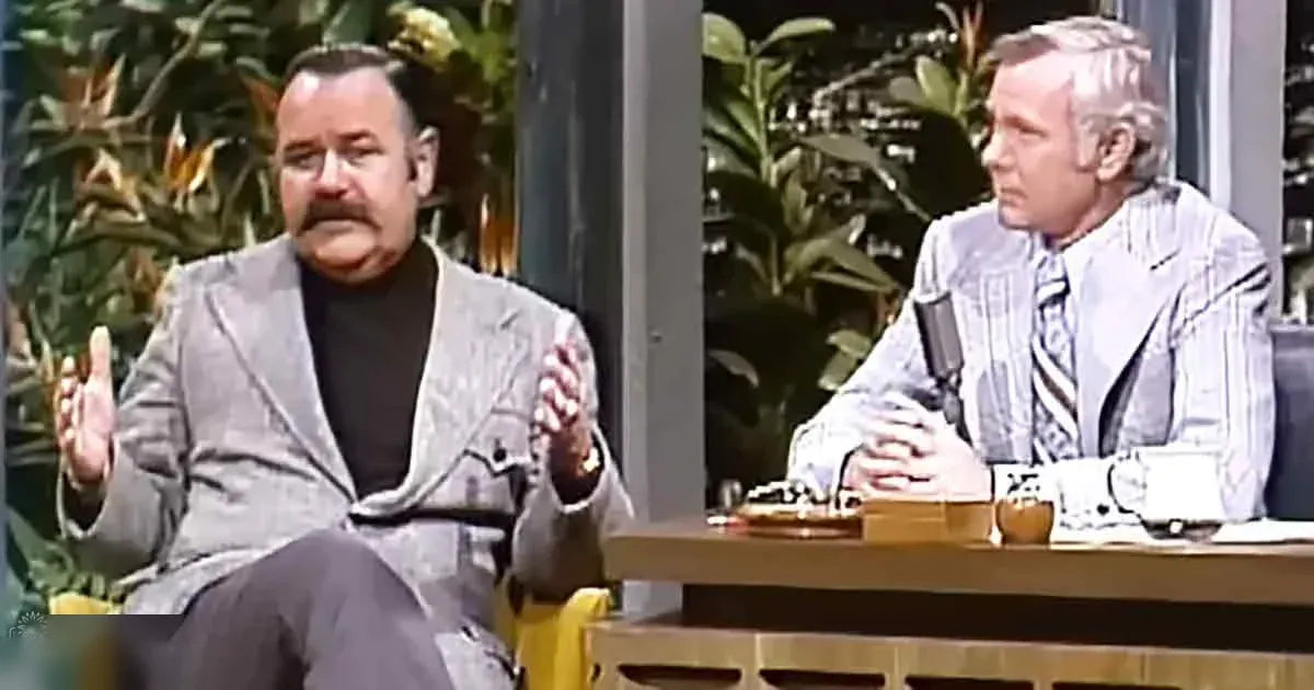 Middle-aged man in a casual interview setting with relaxed attire and plants in the background suggesting a late 20th-century talk show environment.