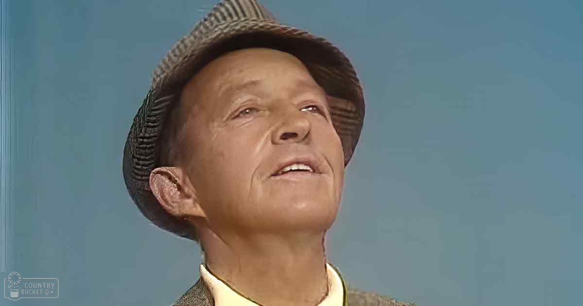 Older adult male wearing a dark-striped fedora and light yellow collar in a studio setting, text 'Madly Odd' watermark visible.