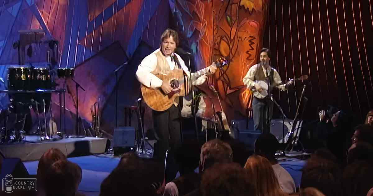 A musical performance in an indoor venue with performers dressed in light and dark clothing, set against abstract autumn-themed backdrop under stage lighting.