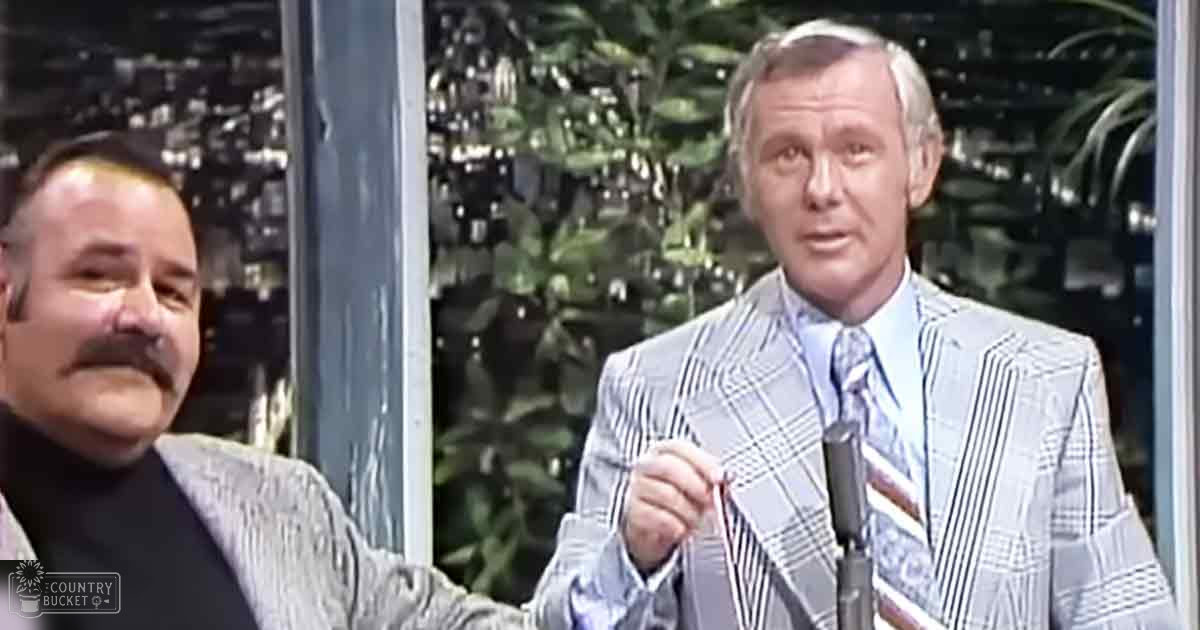 Two older adult men dressed formally indoors with greenery visible through large windows suggesting daytime and spring or summer ambiance.