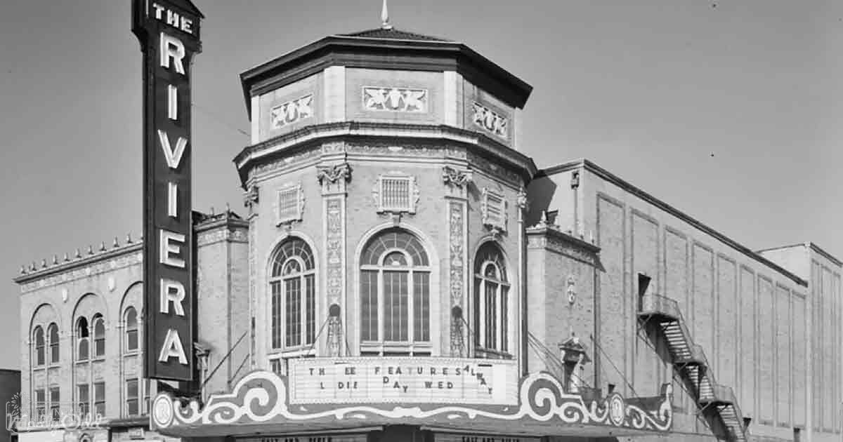 Ornate theater with 'THE RIVIERA' signage in an urban setting, daytime conditions, black and white image