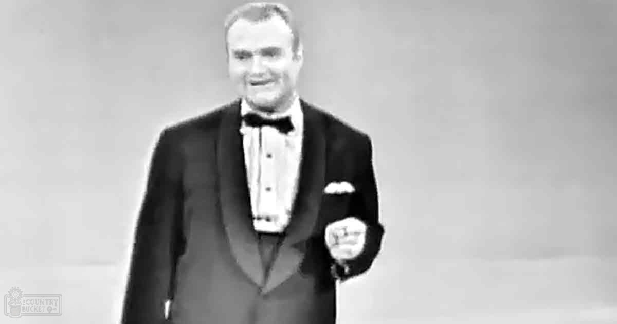 A middle-aged adult male wearing a classic tuxedo with a bow tie, set against an indoor backdrop with soft lighting.
