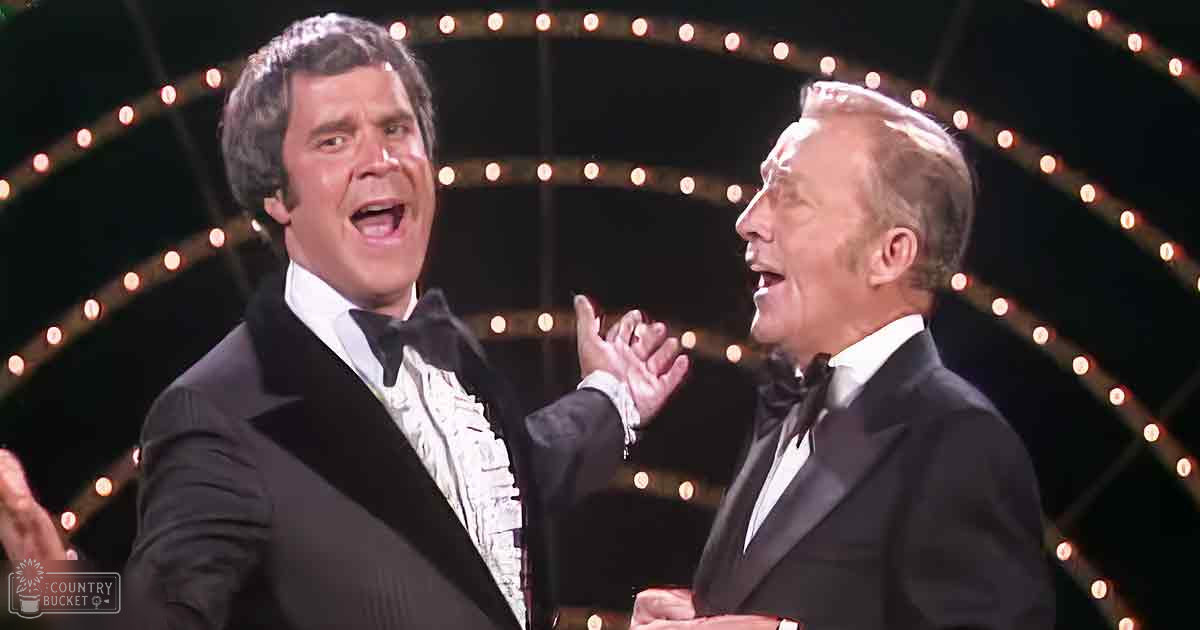 Two adult men in classic black tuxedos with white shirts and bow ties perform a duet on what appears to be a stage set during an evening performance.