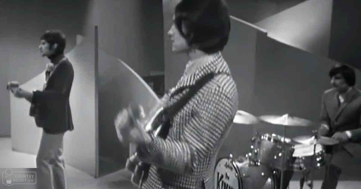 Young adults playing music in an indoor music studio with soundproofing panels and a drum set visible.