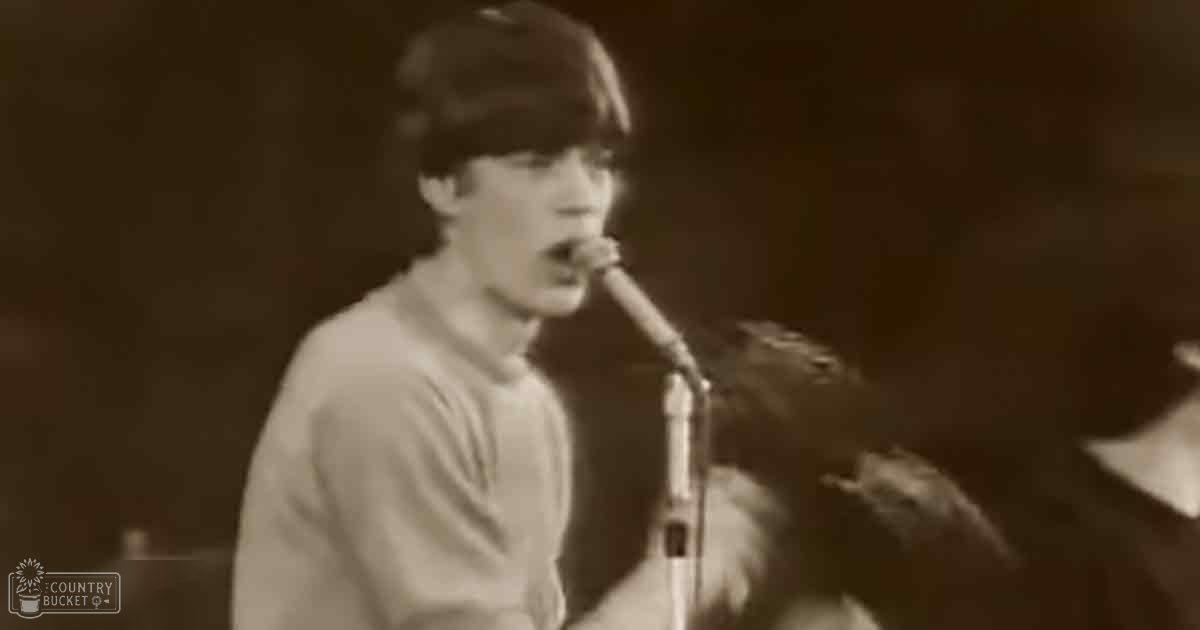 A young adult male singing into a microphone at an indoor live music performance with a vintage sepia tone.