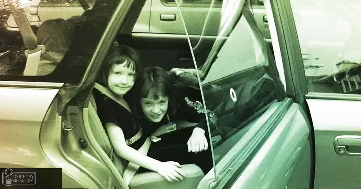 Two children in dark patterned tops inside an open car door, likely parked indoors, under artificial lighting.