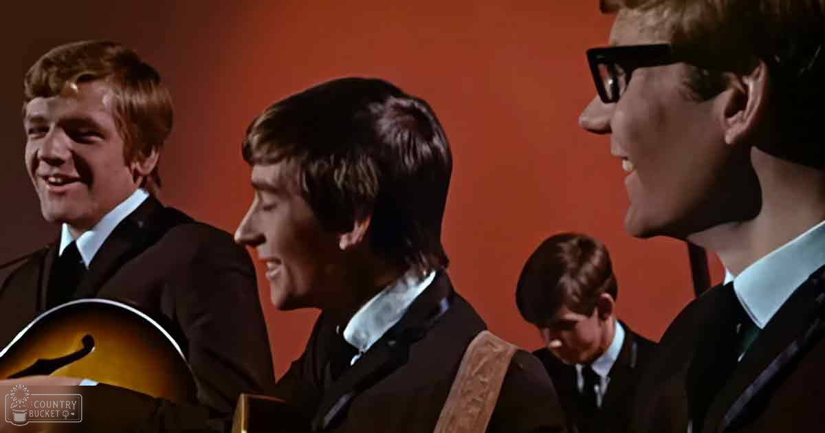 Young adult males in formal attire stand together against an orange background within a studio setting.