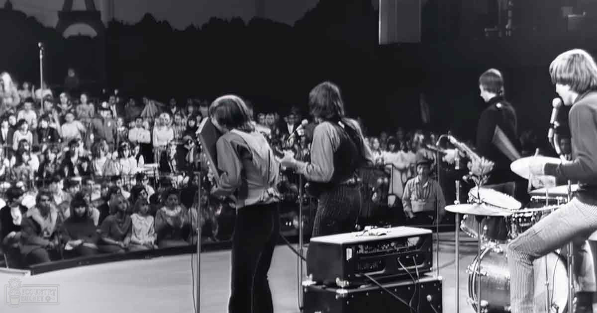 A musical performance with a band playing on stage in front of an audience at an indoor concert venue.