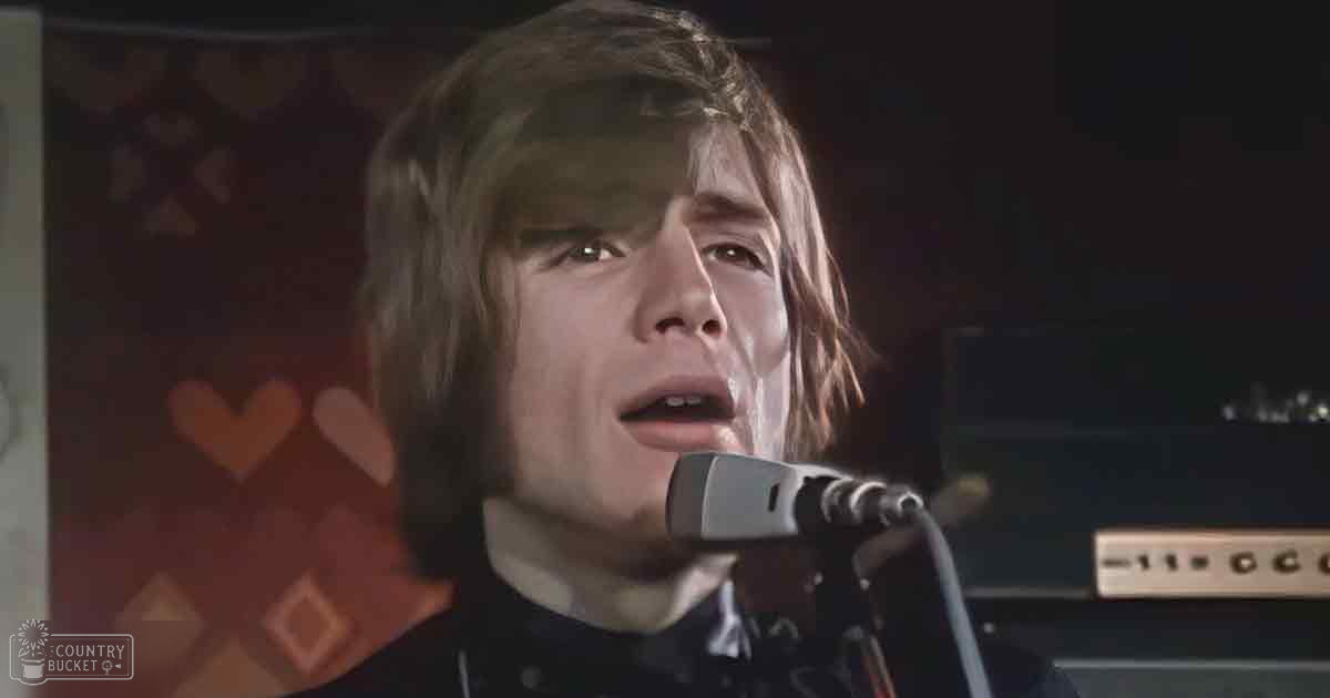 A young adult male sings into a microphone in what appears to be a music studio setting.