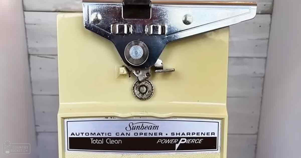 Vintage Sunbeam Automatic Can Opener Sharpener Total Clean Power Pierce, mid-20th century design, beige body with silver metal parts, black text on label, indoor setting possibly kitchen or storage area.