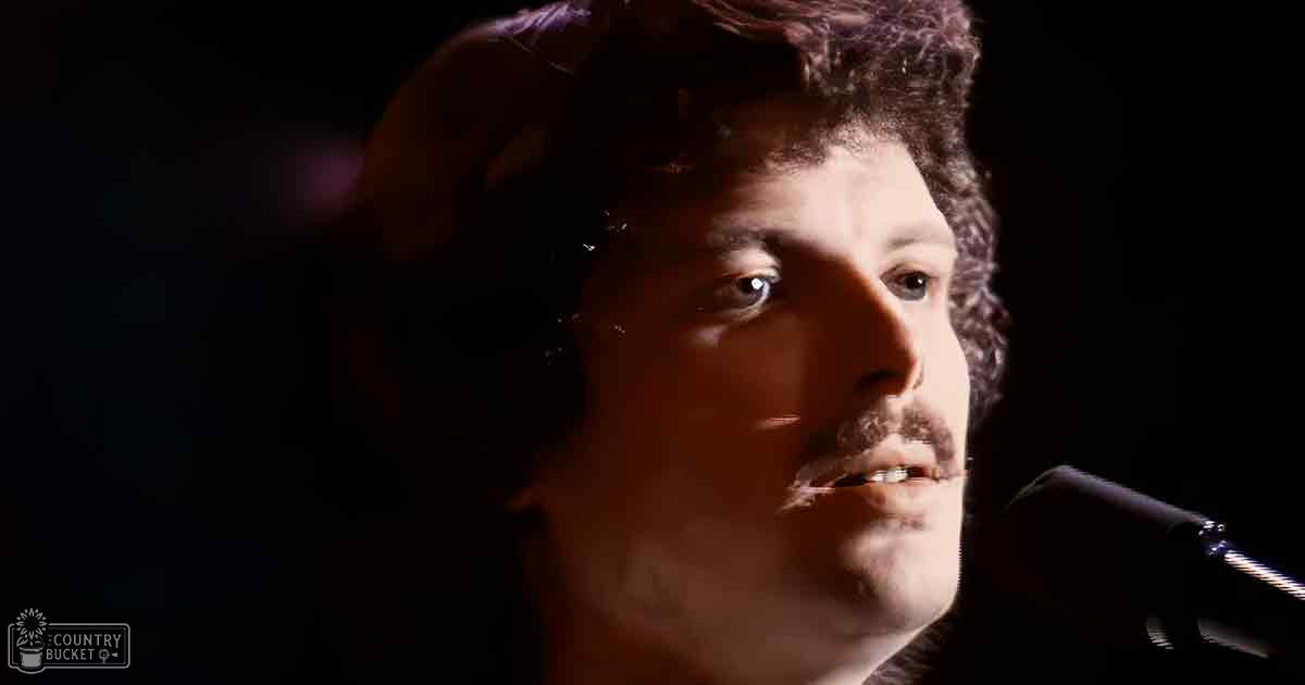 A young adult male singer in casual attire performs into a microphone under dramatic indoor lighting.