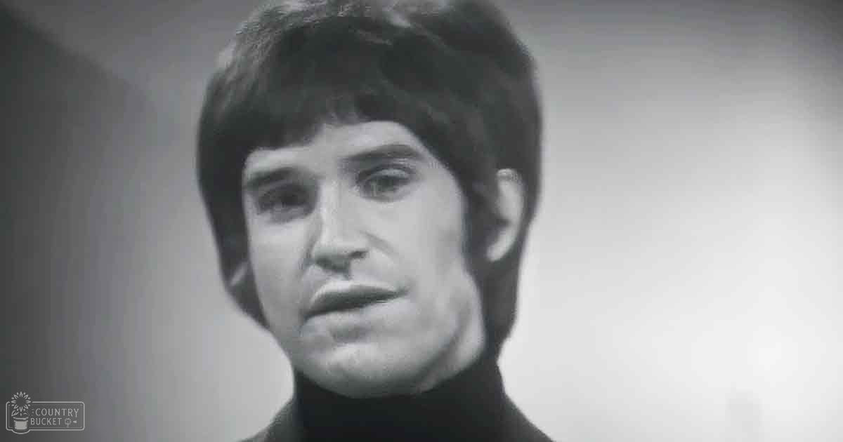 A young adult male wearing a black turtleneck sweater in an indoor setting with plain walls.