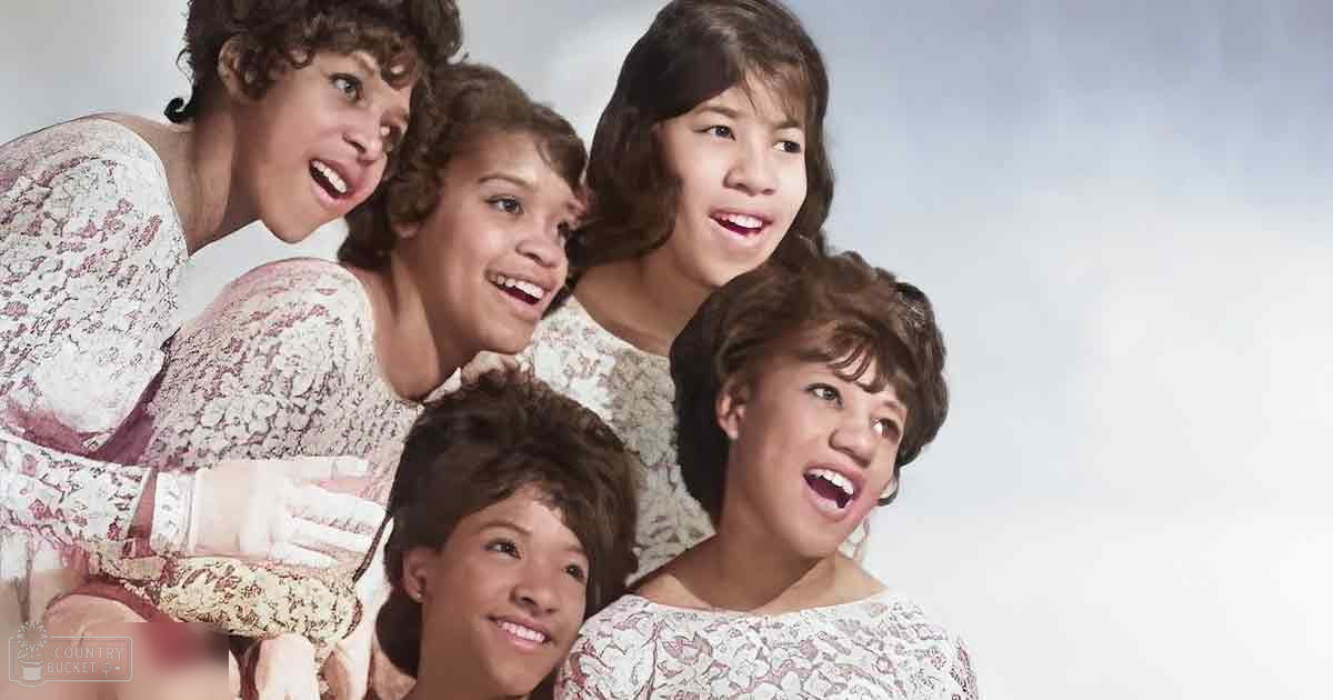 A family group in an indoor setting; children wearing similar floral-patterned dresses against a plain background