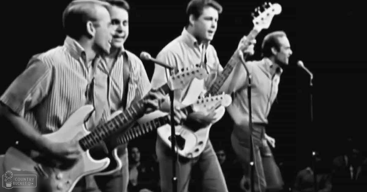 Young adult male performers wearing striped shirts on a stage with microphones, dark indoor venue, artificial lighting, monochromatic setting.