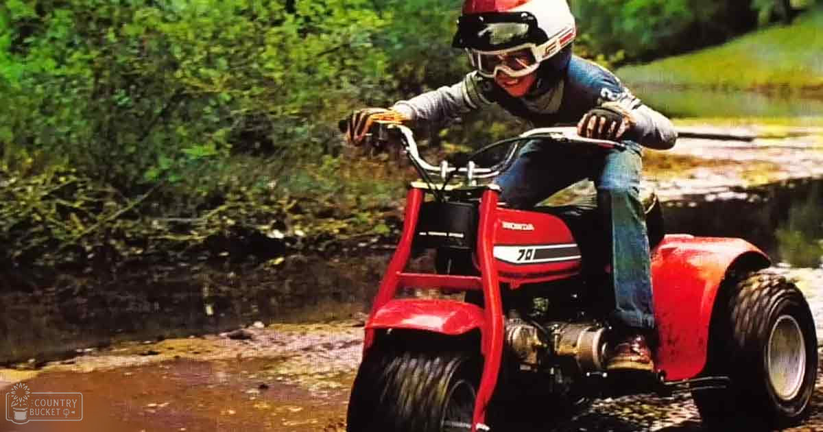 An adult male wearing vintage outdoor activity gear rides an ATV on muddy terrain in a lush green natural setting with spring or summer light.