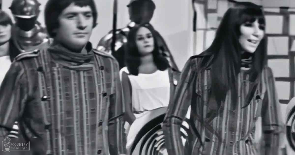 Young adults in a medieval castle setting, dressed in late 1960s or early 1970s fashion, with natural daylight illuminating the scene.
