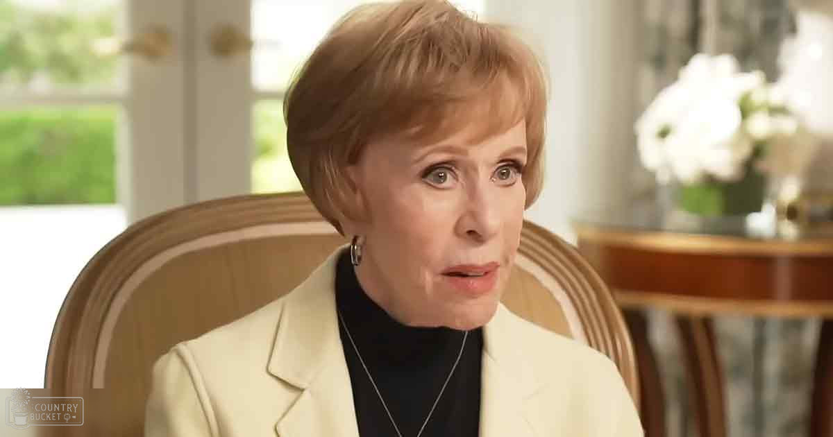 An older adult female wearing a tailored beige blazer over a black turtleneck sweater in an indoor formal setting with natural light.