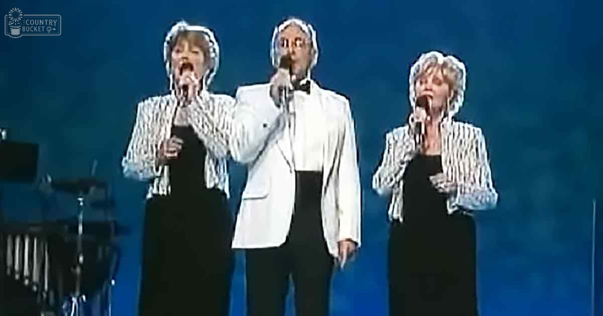 Middle-aged female performer in a black dress with a white patterned jacket over it on stage performing at an event or concert.