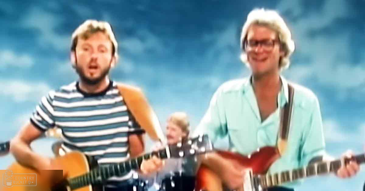 An outdoor musical performance scene with three adults wearing casual summer attire, set against a bright blue sky and white clouds.