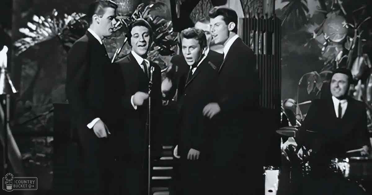 A musical performance scene with a stage set against tropical foliage under bright lighting.
