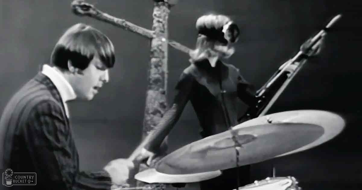 A mid-20th century musical performance scene with performers wearing dark jackets and suits on a stage under dramatic lighting.