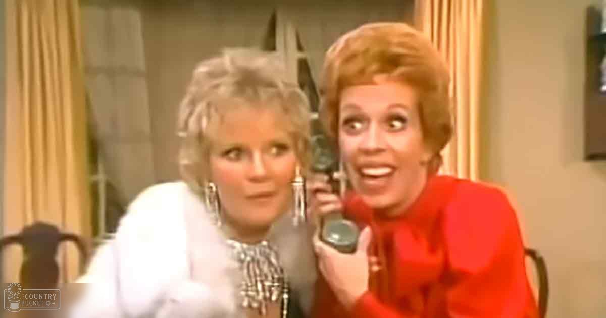 Two women, one wearing a white checkered blouse with mid-20th-century style, another in a bright red high-necked garment, seated in an indoor studio setting with curtains and microphones visible.
