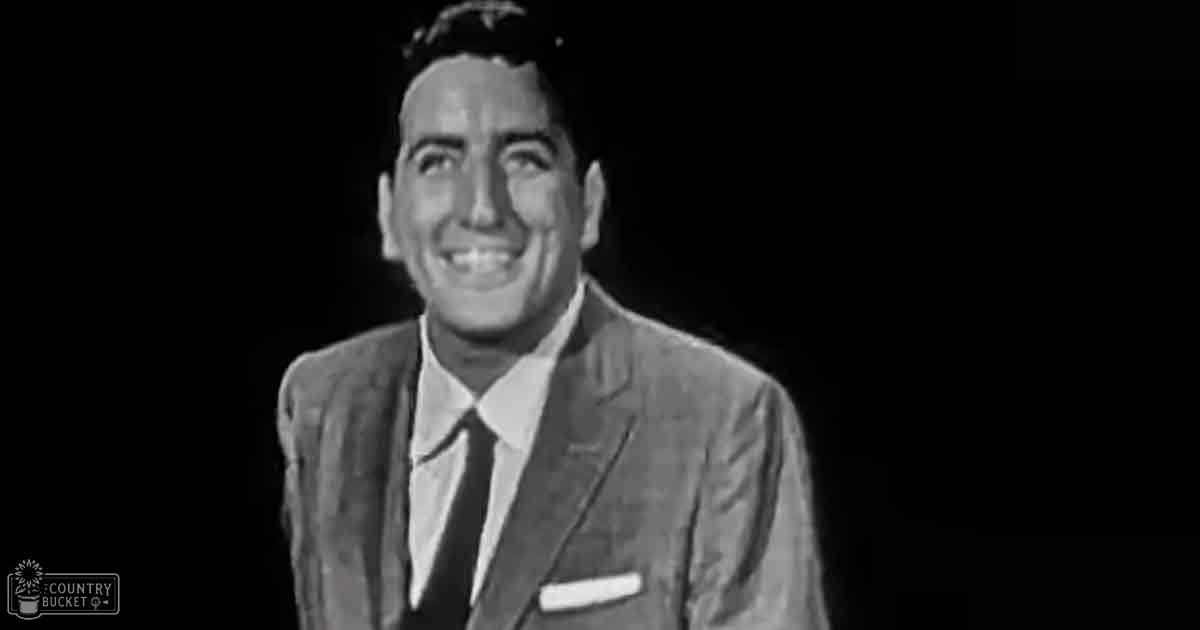 Adult male wearing a well-fitted suit jacket with classic mid-20th century style, indoors against a dark background.