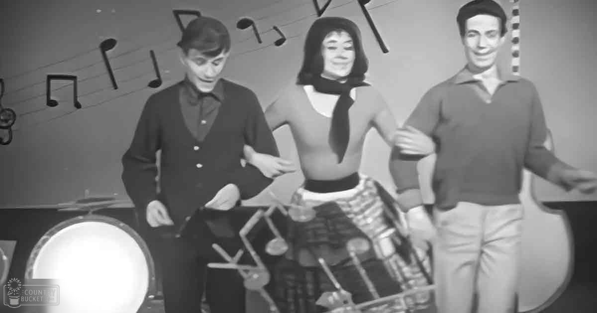 A musical performance scene in an indoor studio setting with three young adults dressed formally with a drum set and musical notes on the wall.
