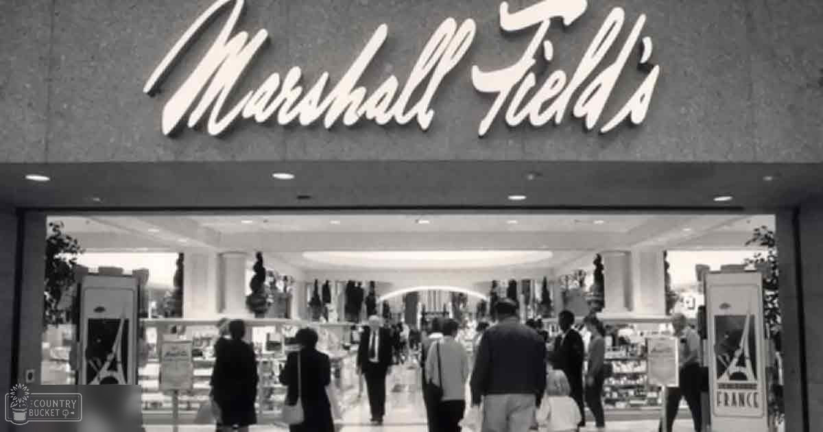 Marshall Field's store front in a shopping mall with an adult male singer wearing a dark suit, an adult female passerby in a light-colored coat and dark dress, and another adult male in a dark jacket. The setting includes interior elements of the store such as clothing racks and displays under artificial lighting.
