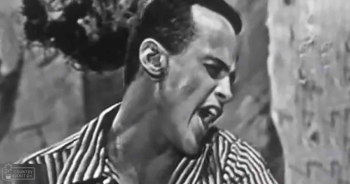 A young adult male in an outdoor setting, wearing a relaxed tunic-style striped shirt with long sleeves and a collared neckline.