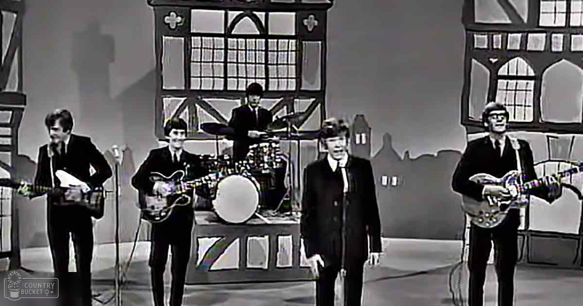 A stage resembling an English countryside, with a drum set and microphones for band members dressed in dark suits.
