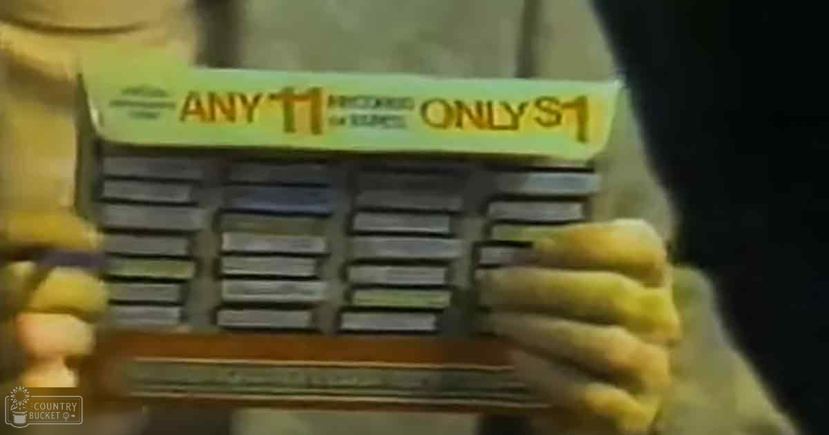 Hands holding a stack of late 20th-century cassette tapes labeled 'ANY 11 PRODUCED FOR LESS ONLY $1', set in an indoor environment with yellow and black label colors.