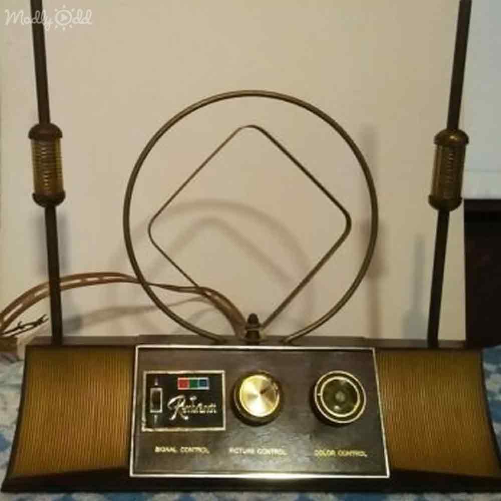 An old-fashioned television with two vertical antennas and a circular top, set against a plain white background in an indoor setting.