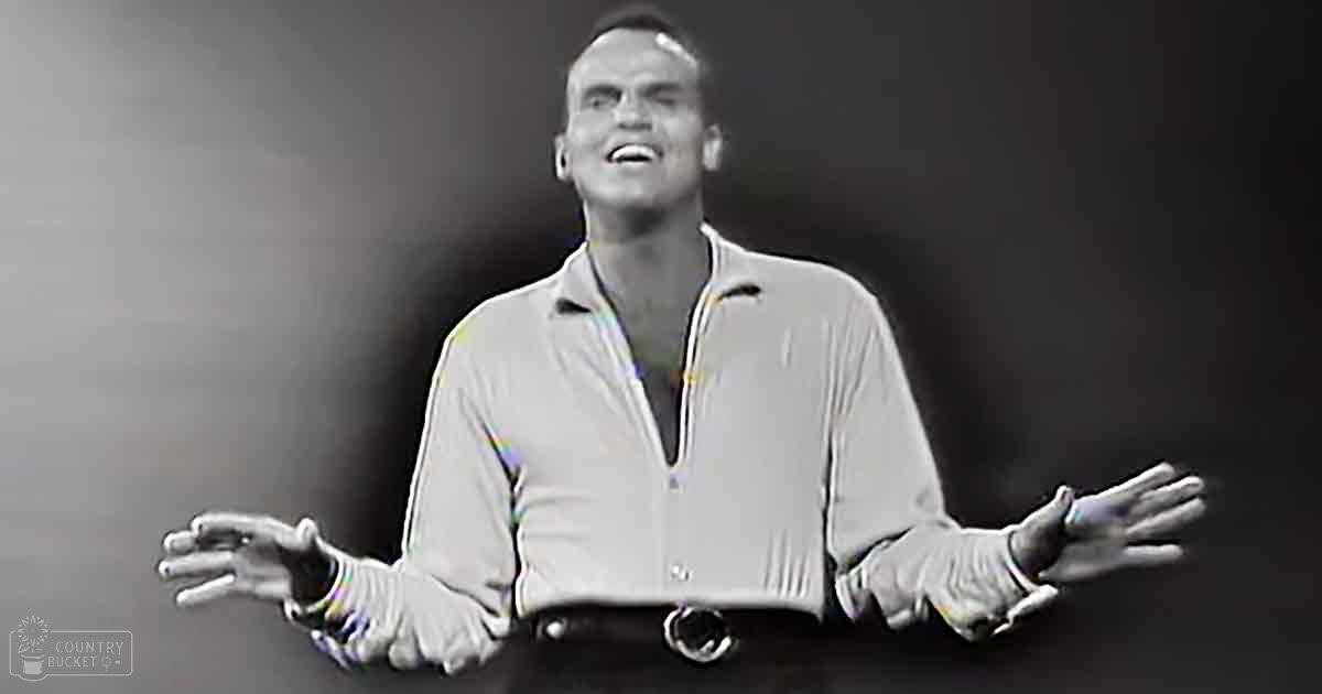 Adult male singer wearing a long-sleeved, collared shirt with zipper and belt in a studio setting. 'Madly Odd' text visible.