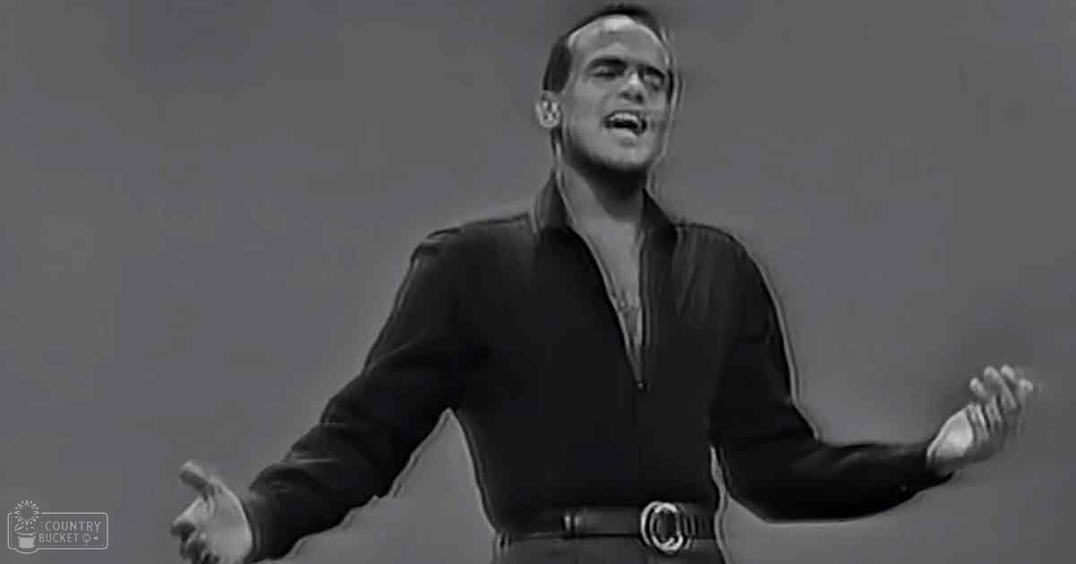 A young adult male singer in a dark-colored long-sleeved shirt performing on an indoor stage at night.