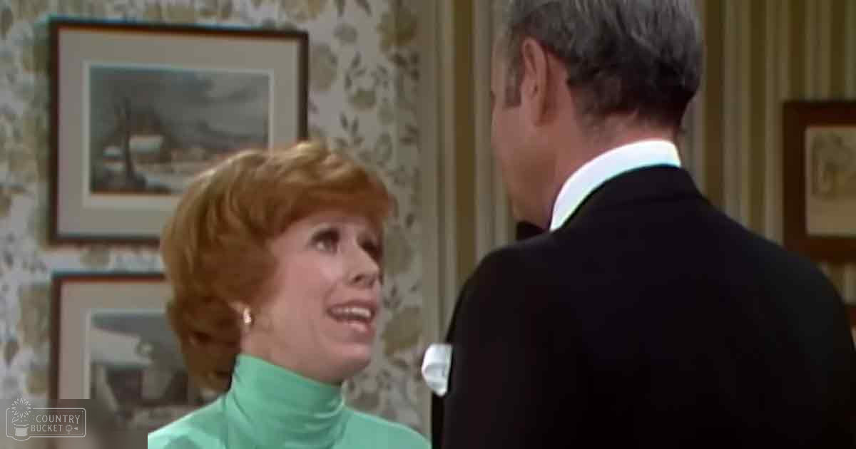 An adult female in a light green turtleneck sweater stands indoors with floral wallpaper and framed winter landscapes; an adult male in a dark suit jacket is also present, suggesting a mid-20th century domestic setting.