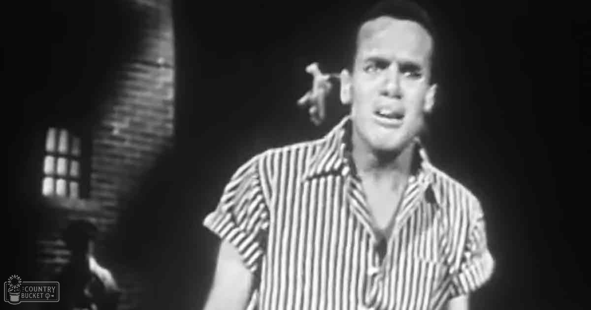 A young adult male wearing a striped short-sleeved shirt indoors with brick walls and dim lighting, possibly at night.