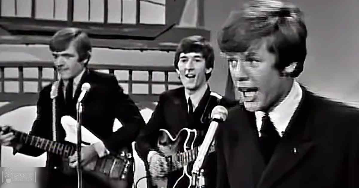 A mid-20th century musical performance scene in a studio with young adult male singers wearing dark tailored suits, playing guitars and singing into microphones under bright even lighting.