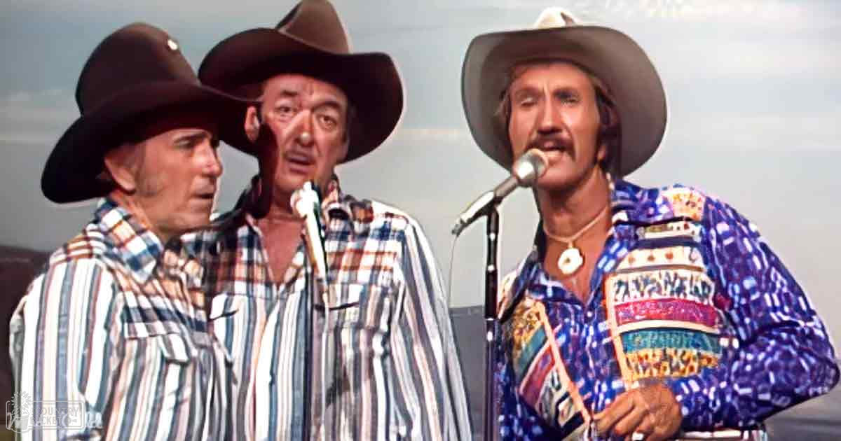 Musical performance by adult males in plaid shirts and cowboy hats under an overcast outdoor sky.