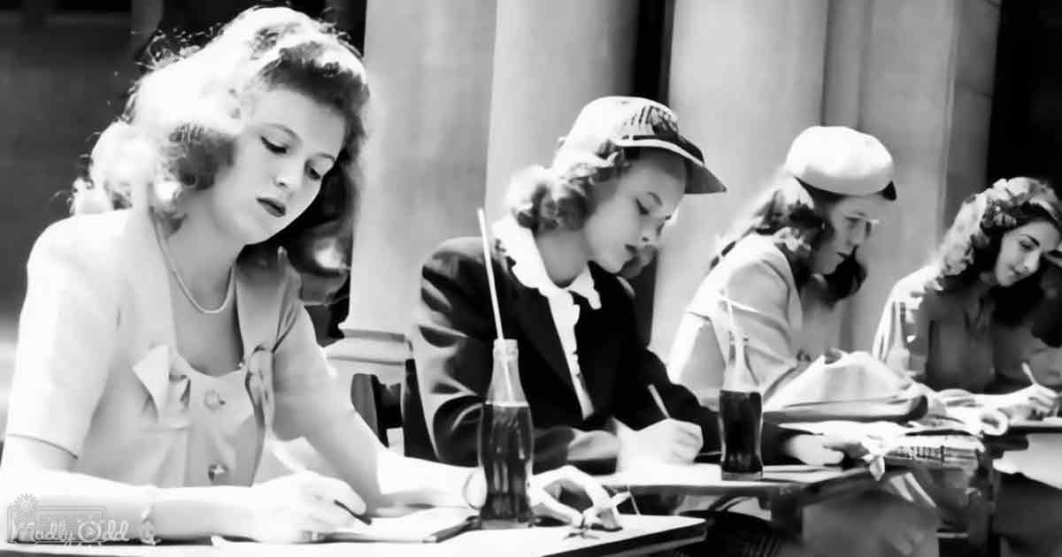 An older era classroom setting with young adult females in light dresses and dark blazers, simple furnishings, natural daylight, indoor school environment.