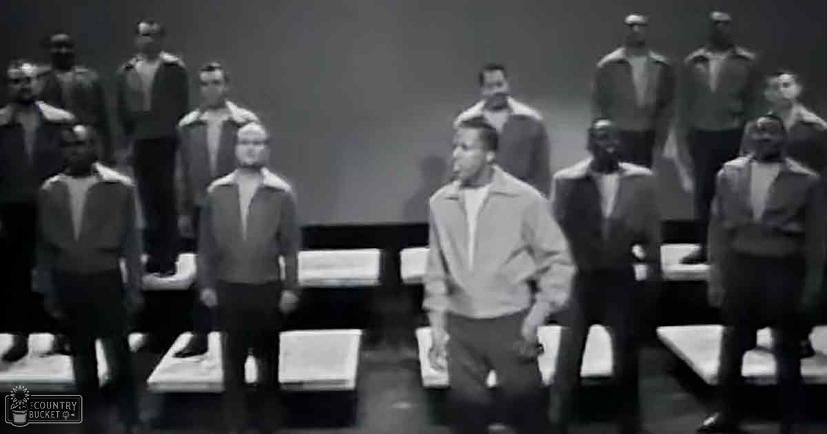 A group of adult males dressed in light-colored jackets and dark pants arranged indoors under even lighting.