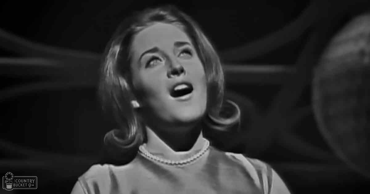 Adult female in a mid-20th century garment with high neckline indoors; evening lighting, dark background.