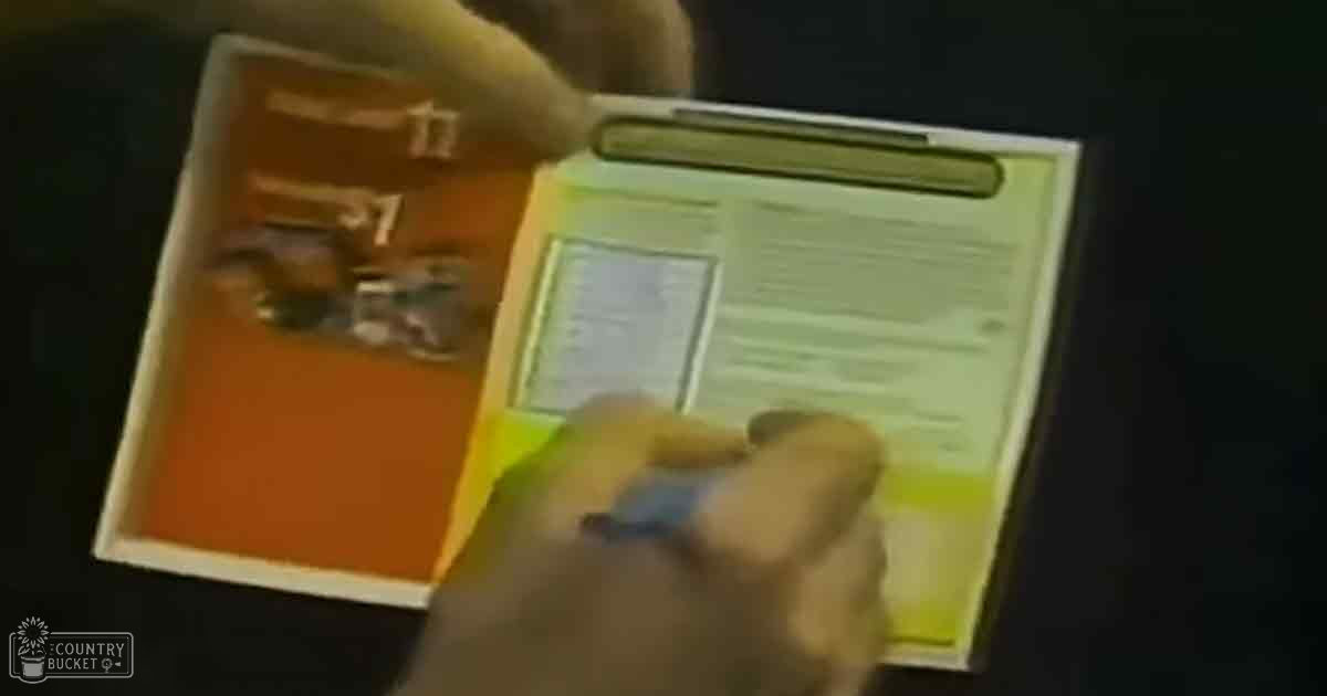 An adult male in a light-colored long-sleeved shirt writing in a notebook with yellow pages and an orange folder, set against a dark indoor background.