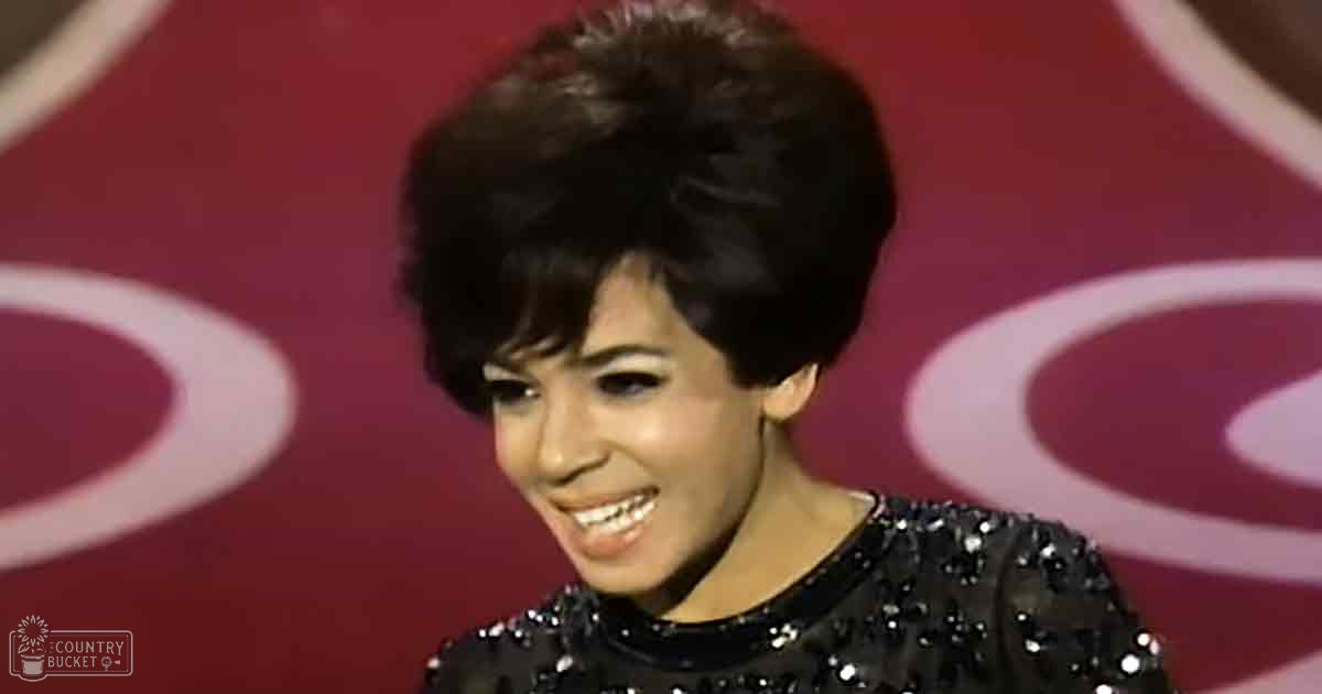 A young adult female in a form-fitting, vintage-style sequined dress at an indoor event or performance with a red backdrop.