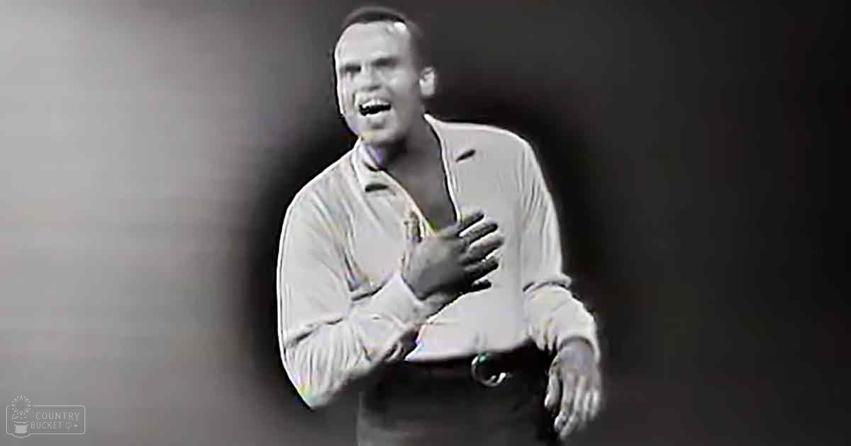 A young adult male wearing a mid-20th-century style button-up shirt indoors with hands clasped near chest in spotlight effect, black and white image.