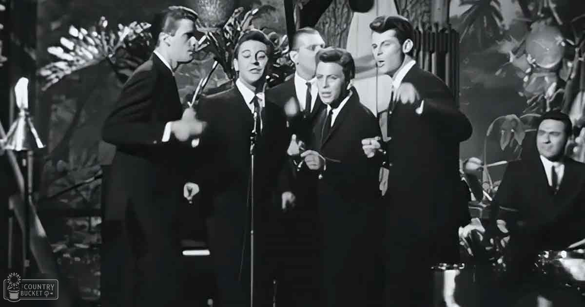 A mid-20th-century musical performance group on stage with tropical backdrop and microphones visible.